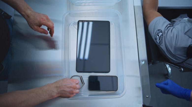 A man places his phone and tablet in a plastic bin at a TSA checkpoint.