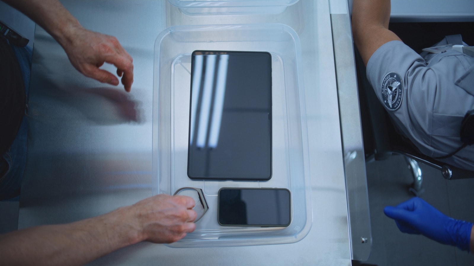 A passenger placing items into a plastic airport security bin.