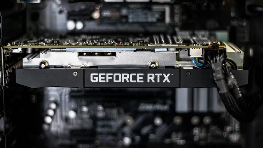An Nvidia GeForce RTX graphics card installed inside a desktop PC, with a power cable plugged in and the motherboard blurred behind it