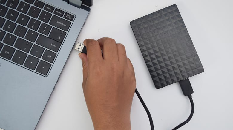 A hand plugging an external hard drive into a laptop via USB.