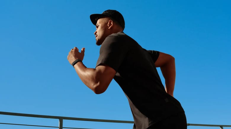 A man running with blue sky in the background and wearing a black Fitbit Air.