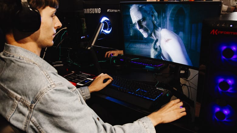 A man playing at a desk on a gaming PC with a scary figure on-screen.
