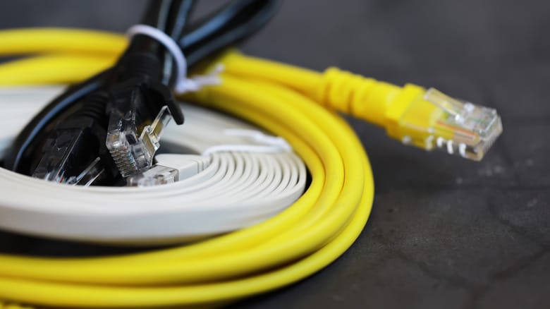 A collection of Ethernet cables stacked on top of each other in black, flat white, and yellow.