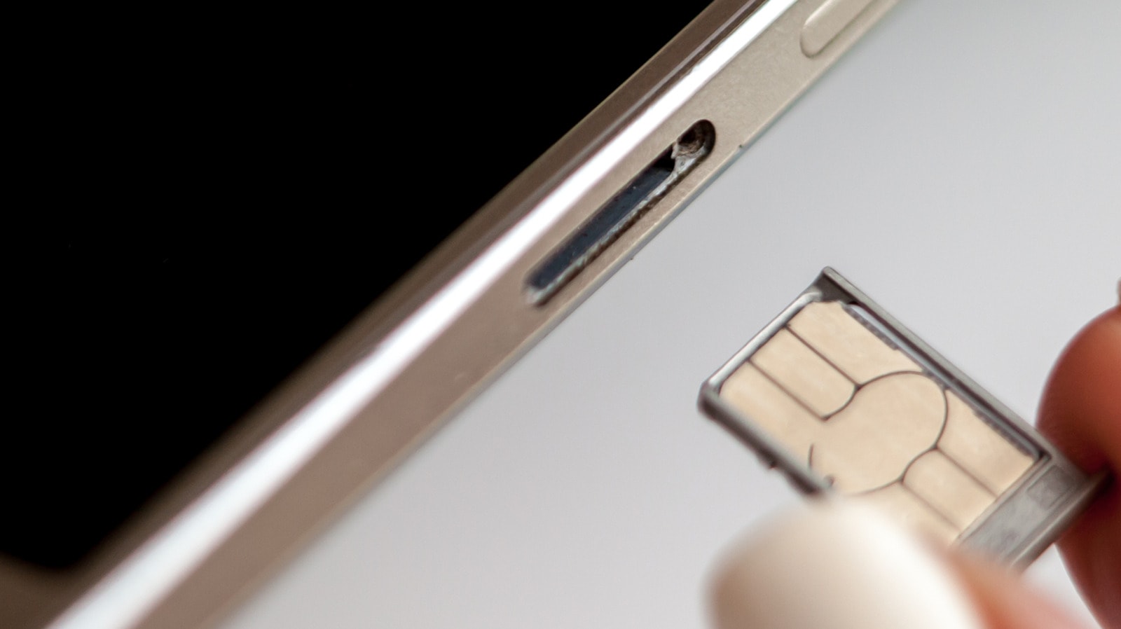 A close-up of a hand inserting a SIM card into a smartphone tray.